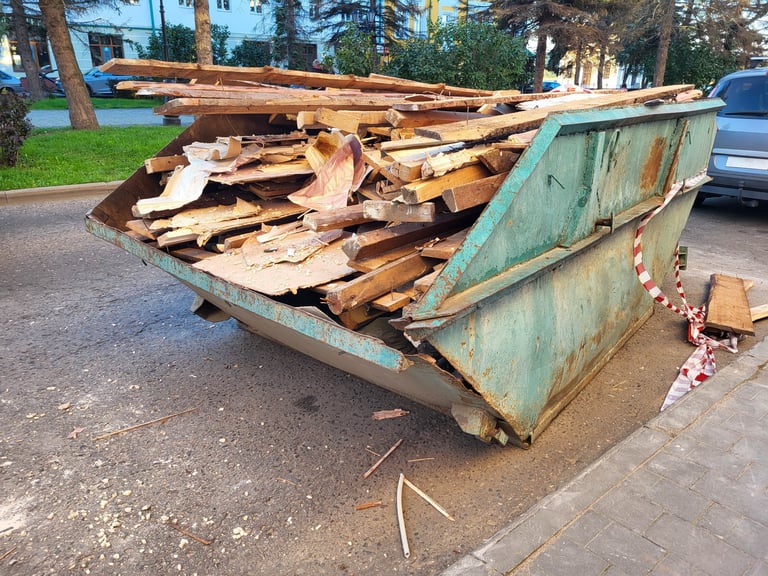 A large green open-top industrial waste container filled with construction debris
