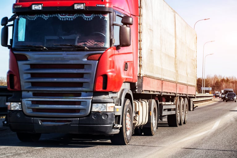 View of red long-haul truck with canvas trailer driving on multi-lane road